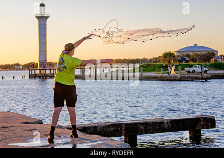 Ein Mann wirft einen Brill net im Broadwater Beach Marina als die Sonne auf Leuchtturm der Marina, 24.02.2019, in Biloxi, Mississippi. Stockfoto