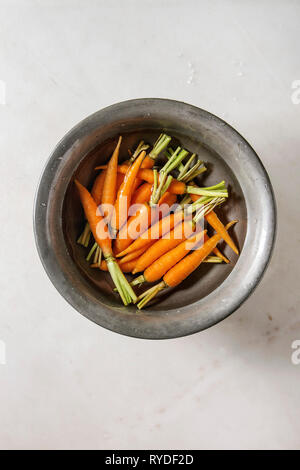 Junge mini Karotte in Wasser in Vintage metall Schüssel über weißem Marmor Hintergrund. Flach, Platz. Kochen, essen Hintergrund. Stockfoto