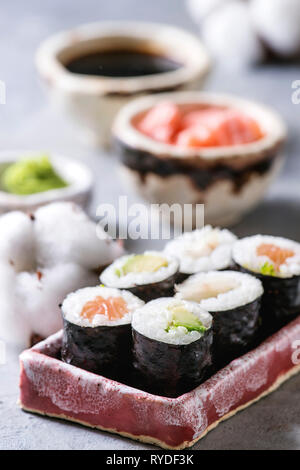 Sushi Rollen in rosa Keramik Servierteller mit Schalen aus Sojasoße und Essig eingelegte Ingwer, Baumwolle Blumen auf hellblau Tabelle. Japan Menü. Nahaufnahme Stockfoto