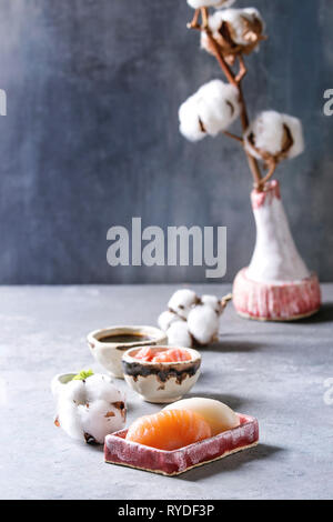 Sushi Set nigiri mit Lachs und butterfisch in rosa Keramik Servierteller mit Schalen aus Sojasoße und Essig eingelegte Ingwer, Baumwolle Blumen auf Hellblau tab Stockfoto