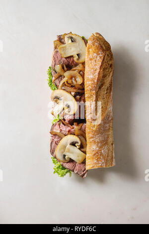Rindfleisch baguette Sandwich mit Champignon Pilze, grüner Salat, gebratenen Zwiebeln mit Zutaten oben auf weißem Hintergrund. Flach, Raum Stockfoto