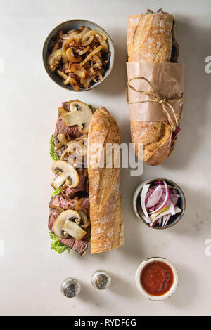 Geöffnet und gebunden Rindfleisch baguette Sandwich mit Champignon Pilze, grüner Salat, gebratenen Zwiebeln mit Zutaten in Schalen auf weißem Hintergrund. Fla Stockfoto