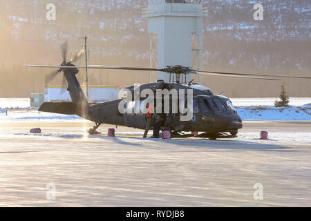 Alaska Nationalgarde Start von Bryant Army Airfield auf gemeinsamer Basis Elmendorf-Richardson, Alaska, über eine 1.BATAILLON, 207 Aviation Regiment, UH-60 Black Hawk Hubschrauber mit zwei pararescuemen von der 212th Rescue Squadron, 176 Flügel, und eine Armee critical care Flug Sanitäter von Abteilung 2, Golf Company, 2. Allgemeine Unterstützung Aviation Battalion, 104 Regiment, an Bord weiter Suche-und-Rettungsaktionen für eine fehlende Flugzeuge in der Nähe von regen Pass, 12. März 2019. Die Gardisten wird ein Alaska Air National Guard HC-130J Combat König-II-Flugzeugen aus. Stockfoto