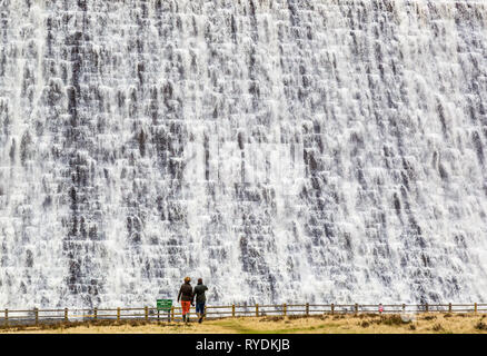 Ein paar zuschauen Wasser überlaufen der Derwent Stausee Staumauer in Derbyshire Peak District nach Wochen von heavy rain Stockfoto