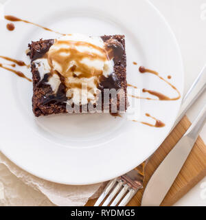 Chocolate Brownie mit einer Kugel Vanilleeis mod Schokoladensauce auf einem weißen Teller. Ansicht von oben, flach Stockfoto