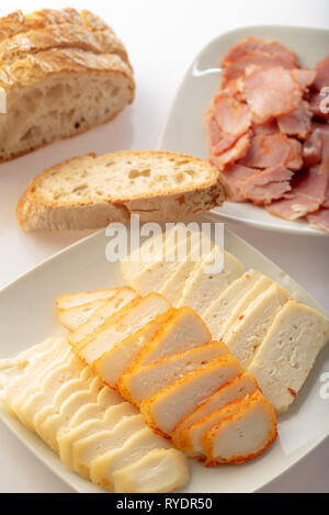 Platte mit verschiedenen Käse mit einer Platte mit Wurst und Brot hinter Stockfoto