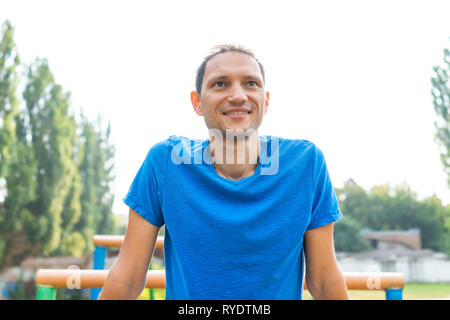 Passen muskulösen Mann Nahaufnahme von Gesicht lächelt glücklich, suchen, calisthenics Workout durch horizontale Balken Barren Übung in outdoor Park in Rivn Stockfoto