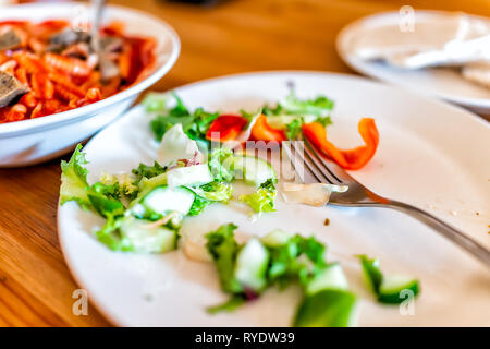 Nahaufnahme des hölzernen Tisch mit unordentlichen Hälfte grünes Gemüse Salat und Platte Gabel Hintergrund gegessen Stockfoto