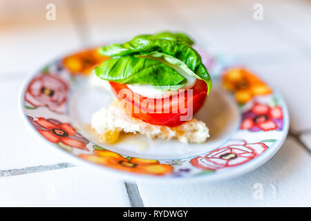 Nahaufnahme von Stück Brot Scheibe auf Platte mit roten Tomaten in Scheiben schneiden und grüne Blätter Basilikum und Mozzarella Käse bruschetta auf Platte Makro auf Fliesen- Zähler Stockfoto