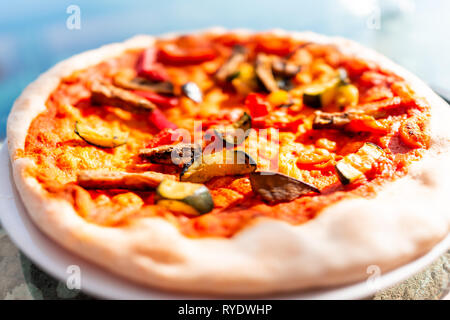 Nahaufnahme der frische Kruste handgefertigte Pizza auf Glas Tisch auf der Terrasse draußen in Italien mit roter Tomatensoße Gemüse lebendige lebendige Farben Stockfoto