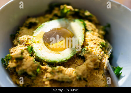Makro Detailansicht von Kale green vegan vegetarisch Salat mit vielen Nährhefe und Avocado Hälfte mit Olivenöl vegane Mahlzeit in der Schüssel gefüllt Stockfoto