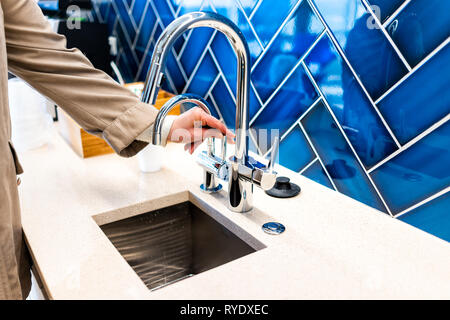 Neue kleine moderne Wasserhahn und Spülbecken closeup mit Frau Drehen am Griff und blau leuchtenden backsplash und glänzend sauber Griff aus Edelstahl Stockfoto