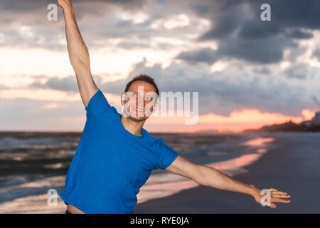 Sonnenuntergang und glückliche junge Mann lächelnd Tanzen in Santa Rosa Beach, Florida mit Küste Küste Küste in Pfannenstiel und Ozean Golf von Mexiko Wellen in Bokeh b Stockfoto