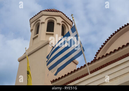 Turm und ein Teil der Bogen Details einer orthodoxen Kirche. Griechische Fahne in den Wind. Bewölkter Himmel. Rethymno, Kreta, Griechenland. Stockfoto