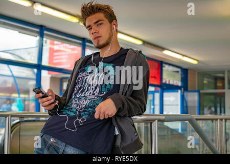 Junge cool Dude Musik auf seinem Telefon, während für einen Freund in einem U-Bahnhof in der Innenstadt von Warschau, Polen warten Stockfoto