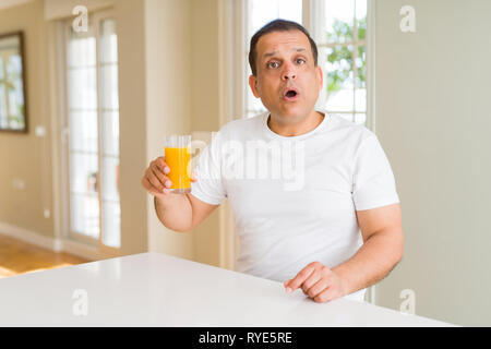 Mittleres Alter Mann trinkt ein Glas Orangensaft zu Hause Angst im Schlag mit einer Überraschung konfrontiert, ängstlich und aufgeregt mit Angst Ausdruck Stockfoto