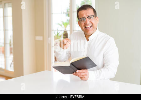Mittleres Alter Mann ein Buch lesen zu Hause Brille sehr zufrieden zeigte mit Hand und Finger Stockfoto