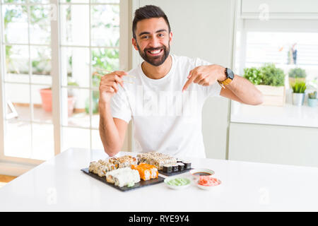 Stattliche Hispanic Mann essen asiatische Sushi mit Stäbchen sehr glücklich zeigte mit Hand und Finger Stockfoto
