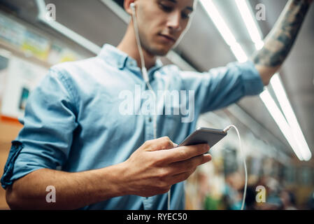 Junger Mann mit Handy in der U-Bahn, Neigung Stockfoto