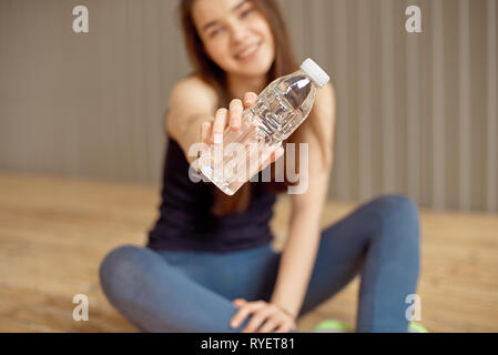 Schöne junge Erwachsene happy woman holding Plastikflasche mit Wasser in der Hand steht in der Nähe der graue Wand und lächelnd Stockfoto