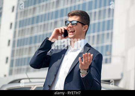 Junger Mann in Sonnenbrille in der Nähe von Auto in Gespräch Lachen Freude Stockfoto