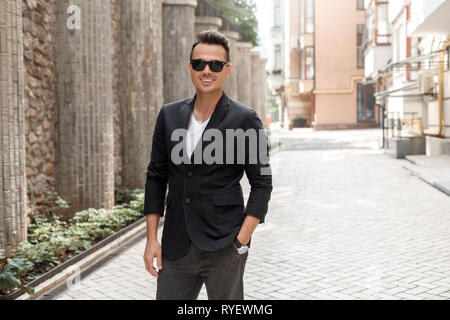 Freizeitaktivitäten im Freien. Junger Mann in Anzug und Sonnenbrille auf der Straße fröhlich lächelnd Stockfoto