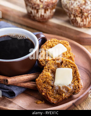Pumpkin Muffin in der Hälfte mit schmelzender Butter und eine dampfende Tasse Kaffee auf einer Holzplatte Stockfoto