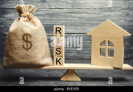 Geld beutel, Blöcke mit dem Wort Risiko und ein Holzhaus auf der Waage. Das Konzept, Geld zu verlieren, wenn Sie in Immobilien investieren. Risiken der Verlust eines Ho Stockfoto