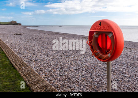 Eine orange lifebouy auf einer verlassenen Budleigh Salteron Strand, Devon, Großbritannien. Der Strand besteht aus Kieseln. Stockfoto