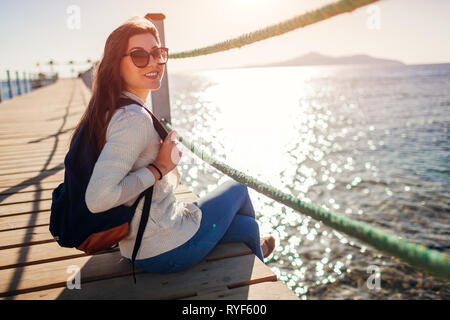 Junge weibliche Touristen mit Rucksack Landschaft bewundern, das Rote Meer und die Insel Tiran sitzen auf Pier. Reisen Konzept. Sommer Urlaub Stockfoto