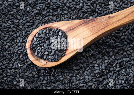 Schwarze Sesamsamen in der Löffel aus Holz. Sesamsamen in die Schüssel im Hintergrund. Ansicht von oben. Stockfoto