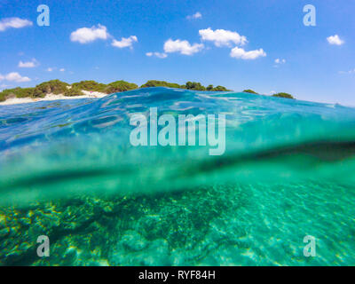 Wundervolle Kristall Türkis und Grün klares Wasser, Sandstrand und blauer Himmel mit einigen Wolken, Unterwasser Blick unter den Wellen Stockfoto