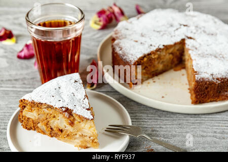 Hausgemachte vegan Apfelkuchen Charlotte, serviert mit einem Glas Tee auf einem Holztisch Stockfoto