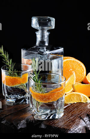 Cocktail classic Dry Gin mit Tonic und Orangenschale mit einem Zweig Rosmarin auf einem Holzbrett mit Scheiben juicy orange Stockfoto