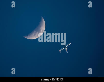 Eines niedrig fliegenden Verkehrsflugzeug passiert einen Halbmond in einem dunkelblauen Himmel bei Sonnenuntergang. Stockfoto