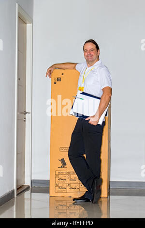 Der Postbote stand neben einem großen Paket auf Korridor von Resident House. Der E-Mail-Dienst trägt eine große Lieferung in die Wohnung. Stockfoto