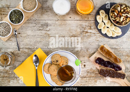 Holztisch zum Süßen Veganes Frühstück Schuß von oben mit Bananenscheiben, gemischte Trockenfrüchte, vegane Kekse, Brot mit Marmelade und veg h Stockfoto