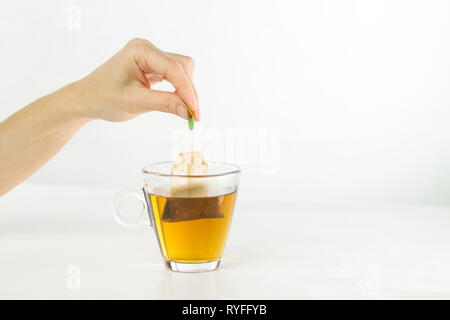 Nahaufnahme einer Frau hand Tauchen einen Teebeutel in ein Glas Schale voll Wasser mit schönen roten Auswirkungen in Bezug auf die Transparenz der Wasser Stockfoto