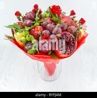 Schönen Blumenstrauß aus Granatapfel, Äpfel, Pflaumen und roten Rosen in einer Vase auf einem Holztisch Stockfoto