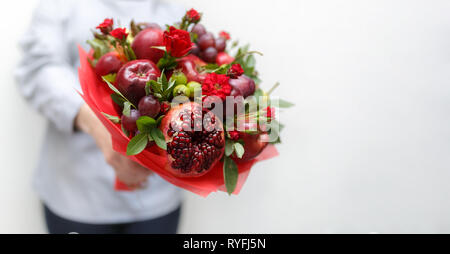 Schönen Blumenstrauß aus Granatapfel, Äpfel, Trauben, Pflaumen und roten Rosen in den Händen einer Frau, die auf einem weißen Hintergrund Stockfoto