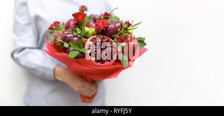 Schönen Blumenstrauß aus Granatapfel, Äpfel, Trauben, Pflaumen und roten Rosen in den Händen einer Frau, die auf einem weißen Hintergrund Stockfoto