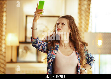 Unglücklich passen Frau mit langen brünetten Haar an moderne Home versuchen, bessere WLAN-Signal auf dem Smartphone erhalten.
