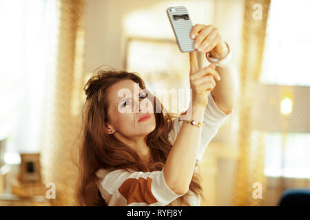 Unglückliche junge hausfrau mit langen brünetten Haar in der modernen Wohnzimmer mit wlan Low-signal Problem auf dem Smartphone.