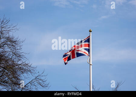 Eine Union Jacl fliegen vor blauem Himmel und leichtem wispy Wolken und Ästen auf der linken Seite Stockfoto