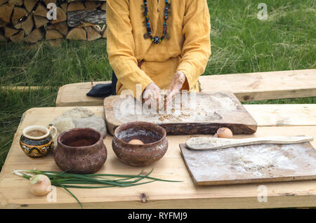 Weibliche Hände brechen ein Ei in einen Haufen von ganzen Körnern Mehl auf ein Brett beim Vorbereiten der handgefertigten Brot Stockfoto