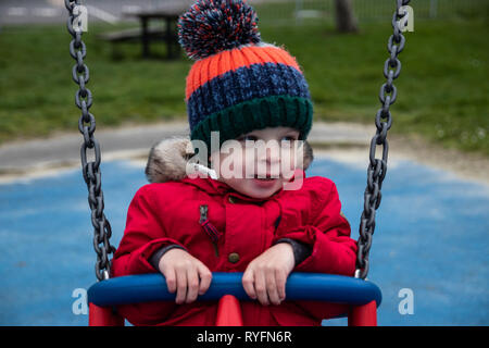 Kleine Jungen im Park Schaukeln im Winter Kleidung Stockfoto