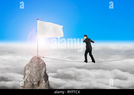 Geschäftsmann wandern und Auswuchten auf Seil in Richtung weiße Flagge von Berg mit cloudscape Sonnenlicht Hintergrund Stockfoto
