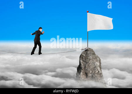 Geschäftsmann wandern und Auswuchten auf Seil in Richtung weiße Flagge von Berg mit cloudscape Hintergrund Stockfoto