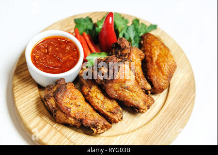 Gegrilltes Hähnchen Schenkel. Das Essen ist auf einem Holzbrett, in der Nähe der Tomatensauce in Schalen, frisches Gemüse und Kräuter. Stockfoto
