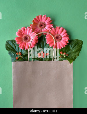 Coral Gerbera daisy flowers und Handwerk papper Einkaufstaschen auf grünem Papier Hintergrund, Frühling Verkauf Konzept Bild mit copy-Raum Stockfoto